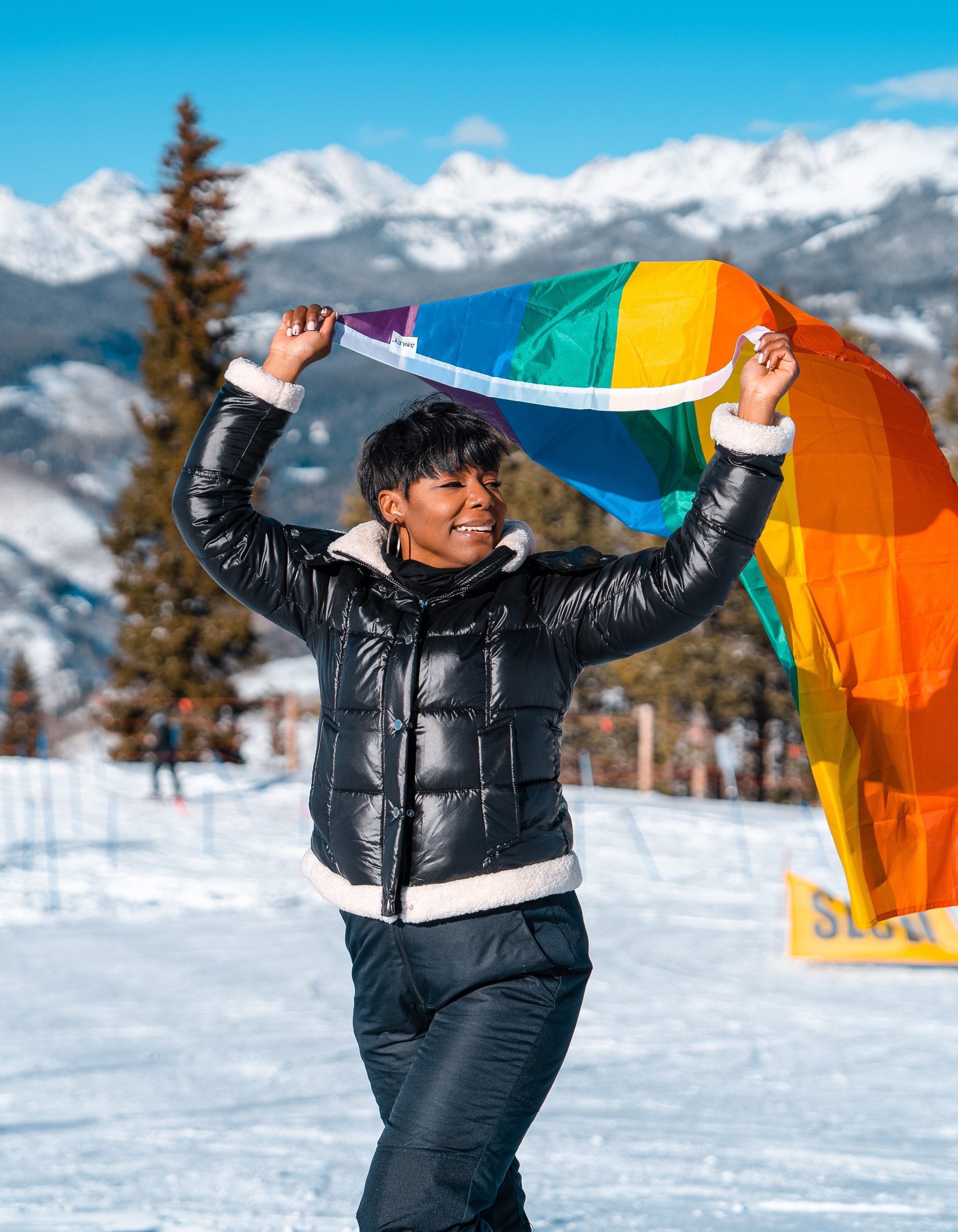 Colby Holiday holding a pride flag overhead on a snowy Vail mountain